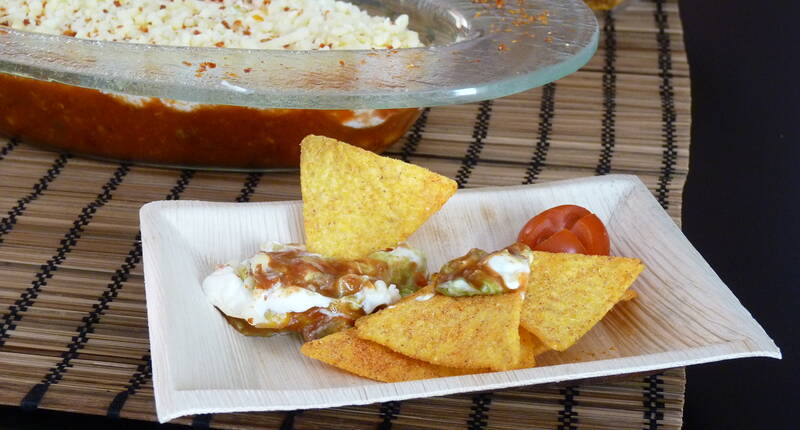 Zutaten für 4 Personen. 1 Avocado. 1 Packung Würzmischung für Avocado-Dip,1 EL Zitronensaft. 1 Tomate. 1/2 Büchse (ca. 200 g) Chili con Carne. 1 Becher Crème fraîche grob geriebener Reibkäse (z. B. Pizza oder Gratin-Mischung) und Tomatenflocken.